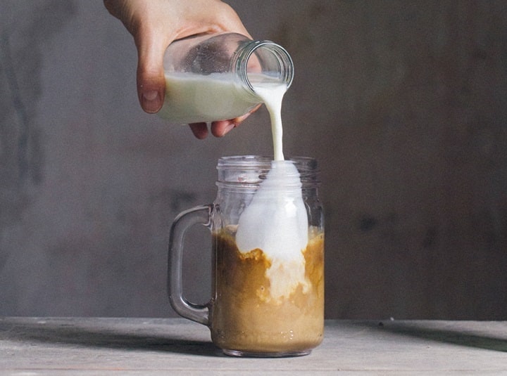 Ręka dolewająca mleko do kawy w dużym kubku
